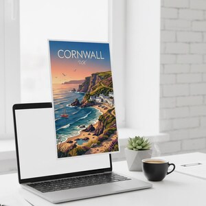 May include: A laptop displays a travel poster for Cornwall, UK, featuring a coastal scene with a red sailboat, cliffs, and a village. The poster is set against a blue sky with the text "Cornwall UK". A succulent and coffee cup are on the desk.