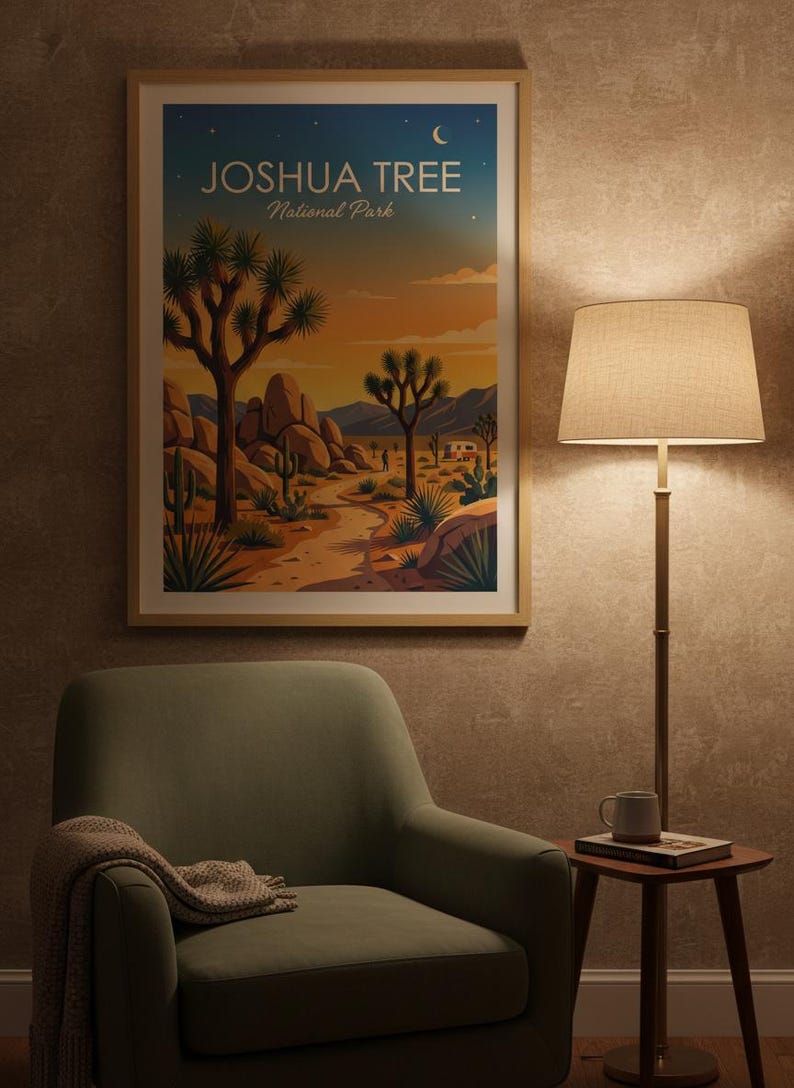 May include: A framed art print featuring a desert landscape with Joshua trees, rocks, and a sunset. The print has the text "JOSHUA TREE National Park" at the top. The print is displayed above a green armchair with a blanket and a side table with a lamp.