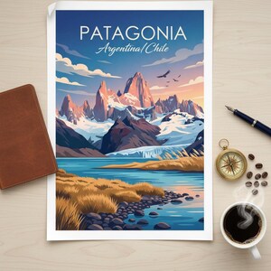 Op de afbeelding: Een Patagonia reisposter met een bergketen en een meer. De poster ligt op een houten oppervlak met een leren notitieboek, pen, kompas, koffie en koffiebonen.