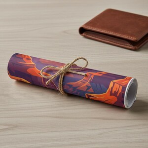 May include: Rolled art print featuring a canyon landscape in shades of purple and orange, tied with twine. A brown leather wallet rests in the background on a light wood surface. The print is a decorative item.