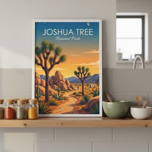 May include: A framed art print featuring a desert landscape with Joshua trees, cacti, and a winding path. The artwork displays the text "JOSHUA TREE National Park" against a sunset sky. The print is displayed on a wooden shelf.
