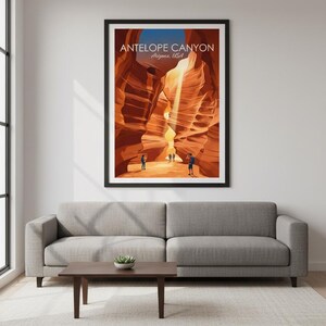 May include: A framed poster featuring Antelope Canyon in Arizona, USA. The artwork depicts the canyon's sandstone walls in shades of orange and brown, with sunlight streaming through. Several figures are visible at the canyon's base. The poster is displayed above a gray sofa.