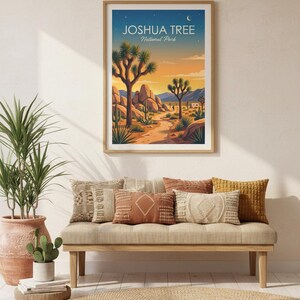 May include: A framed print of Joshua Tree National Park, featuring a desert landscape with Joshua trees, rocks, and a path. The print hangs above a bench with decorative pillows. A potted plant and cactus are also visible.