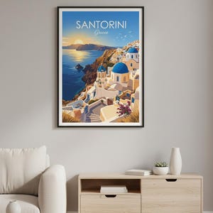 Puede incluir: Impresi&oacute;n enmarcada de Santorini, Grecia. La imagen presenta edificios blancos con c&uacute;pulas azules en un acantilado con vistas al mar Egeo. El cielo es un degradado de azul y dorado, con el texto "SANTORINI Greece" en la parte superior.