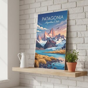Op de afbeelding: Een ingelijste kunstdruk van Patagoni&euml;, Argentini&euml;/Chili, met een bergketen, een meer en een blauwe lucht. De print staat op een houten plank met een witte kan en een plant in een pot. De tekst "PATAGONIA" staat bovenaan.