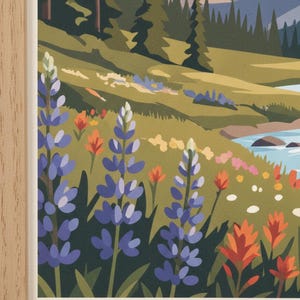 May include: A framed art print featuring a colorful landscape scene. The artwork depicts a mountain range, a river, and a field of wildflowers in shades of blue, orange, and pink. The frame is made of light-colored wood.