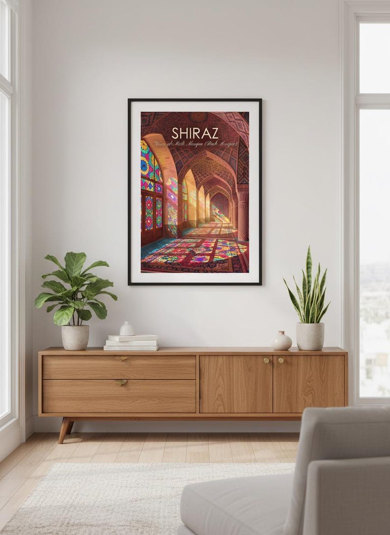 May include: A framed print depicting an arched corridor with stained glass windows and a vibrant carpet. The word "SHIRAZ" is at the top. The print is displayed on a wooden cabinet with plants.