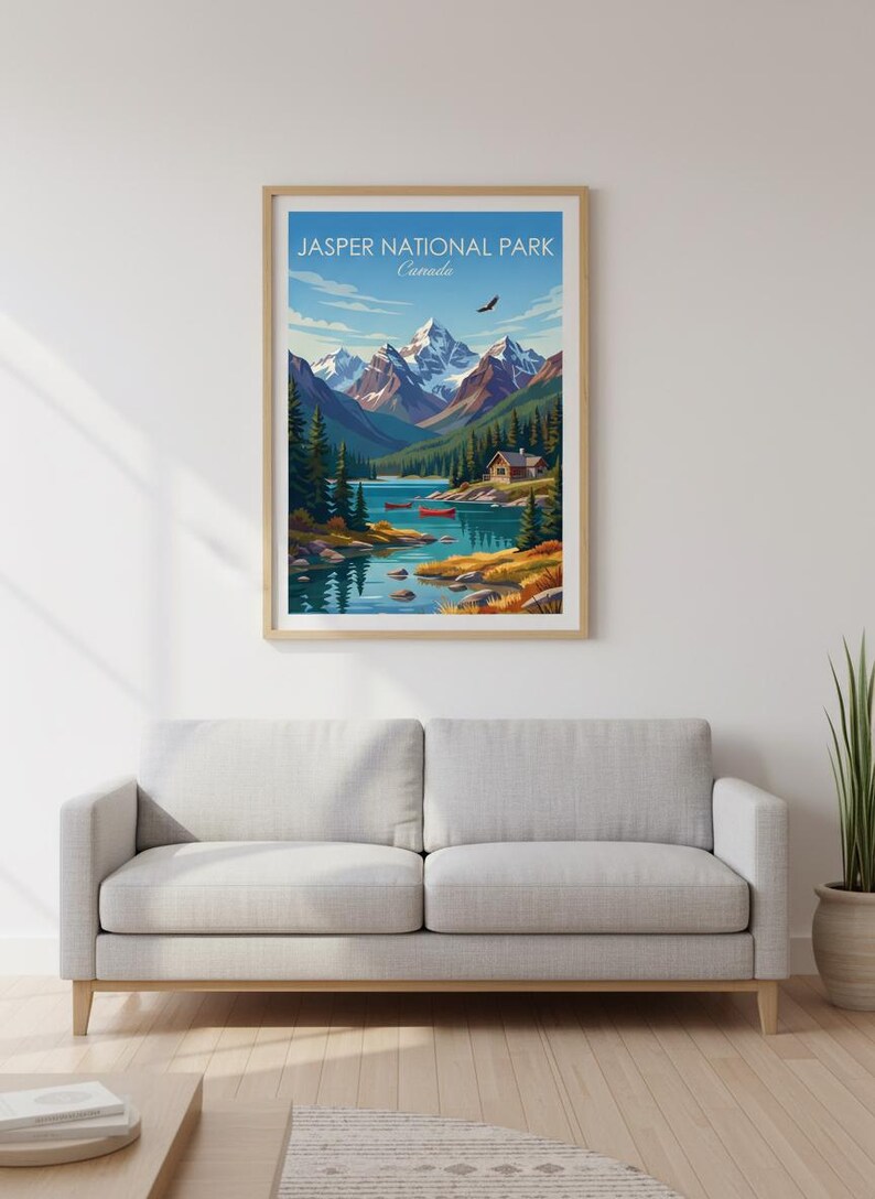May include: A framed print of Jasper National Park, Canada, featuring a scenic landscape. The artwork depicts snow-capped mountains, a lake with red canoes, and a cabin. The sky is blue with a flying bird. The print is displayed above a gray sofa.