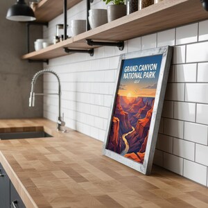 May include: A framed poster with the text "GRAND CANYON NATIONAL PARK USA" depicts a stylized landscape of the Grand Canyon at sunset. The artwork features a river winding through red and orange canyon walls. The frame is silver.