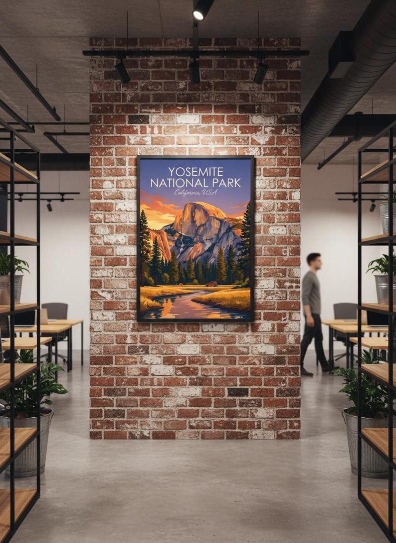 May include: A framed poster featuring a scenic view of Yosemite National Park, California, USA. The artwork depicts a mountain landscape with a river, trees, and a sunset. The poster is displayed on a brick wall in an office setting.
