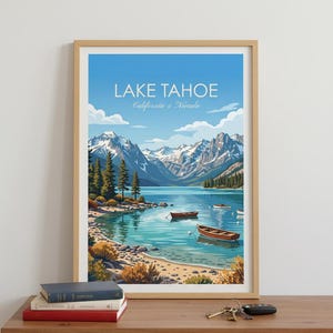 May include: Framed art print of Lake Tahoe, California & Nevada. The image features a serene lake scene with boats, mountains, and a clear blue sky. The artwork is displayed on a wooden table with books and keys.