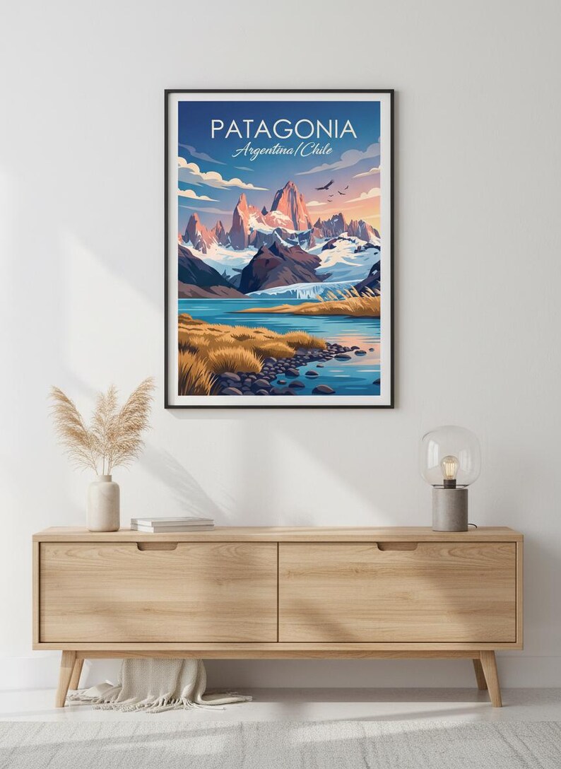 Op de afbeelding: Een ingelijste kunstafdruk met een landschap van Patagoni&euml;, Argentini&euml;/Chili. Het kunstwerk toont besneeuwde bergen, een blauw meer en goudkleurig gras onder een blauwe lucht. De tekst "PATAGONIA" is zichtbaar. De print hangt aan een houten kast.