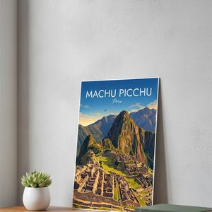 May include: A framed print of Machu Picchu, Peru, featuring a detailed illustration of the ancient city nestled in the mountains. The print has a blue sky background with the text "Machu Picchu Peru". The print is displayed on a wooden surface.