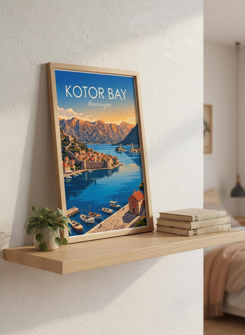 May include: A framed print of Kotor Bay, Montenegro, featuring a vibrant illustration of a coastal town with boats on the water and mountains in the background. The print is displayed on a wooden shelf with books and a small plant.