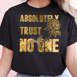 以下が含まれることがあります： ひび割れたメタリックな質感のゴールドの文字で「ABSOLUTELY TRUST NO ONE」とプリントされた黒の半袖Tシャツ。葉と棘のある詳細なゴールドのバラのイラストが「TRUST」という単語の右側に配置されています。