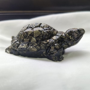 May include: A detailed, dark-colored turtle figurine. The sculpture has a textured shell and a smooth, rounded head. The figurine is set against a white background, highlighting its intricate design and form.