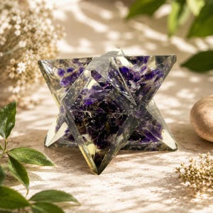 Könnte beinhalten: Eine geometrische sternförmige Skulptur aus klarem Harz, eingebettet mit zahlreichen tiefvioletten Amethyst-Kristallfragmenten. Das facettierte Objekt weist scharfe Spitzen und eine transparente Struktur auf, die die dunklen Steine zeigt.