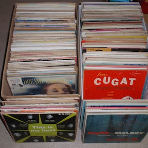 Może przedstawiać: Dwa kartonowe pudełka wypełnione zabytkowymi płytami winylowymi. Płyty mają kolorowe okładki albumów z tekstami, w tym "Xavier Cugat", "Dream" i "This is my best". Płyty są ułożone w rzędach.