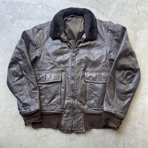 Può includere: Un giubbotto bomber in pelle marrone scuro con colletto in pelliccia sintetica marrone scuro, chiusura frontale con zip, due tasche frontali con patta e bottone, e polsini e orlo in maglia a coste. La pelle presenta una texture vissuta.