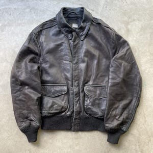 Op de afbeelding: Een vintage zwarte leren bomberjack met een kraag, twee voorzakken en geribde manchetten en zoom. De jas vertoont tekenen van slijtage, wat bijdraagt aan de klassieke uitstraling. Een tijdloos bovenkledingstuk.