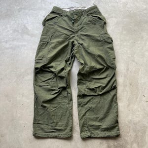 May include: Olive green cargo trousers with multiple pockets and a button and zip fastening. The trousers have a relaxed fit and are made of a durable fabric. The trousers are laid flat on a neutral surface.