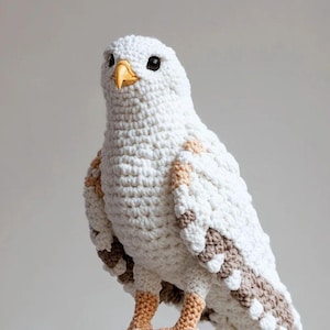 May include: A handcrafted, crochet bird sculpture in white, brown, and tan, perched on a wooden branch. The bird features detailed wings, a yellow beak, and black eyes. The sculpture is a unique piece of home decor.