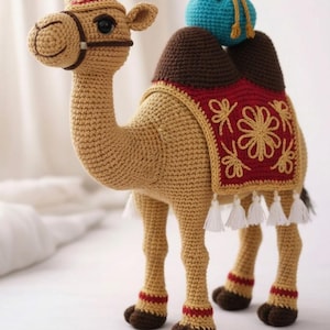 May include: A crocheted camel toy in tan, brown, and red. The camel has a saddle with floral embroidery and white tassels. A small blue pouch sits on its back. The camel has a bridle and decorative trim.