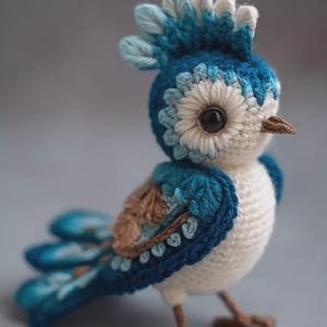 May include: A handcrafted crochet bird in shades of blue, white, and brown. The bird features a detailed head crest, a floral-like design around the eye, and a textured body. The bird is standing on brown crochet feet.
