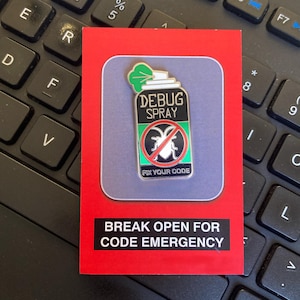 May include: A rectangular pin featuring a green, black, and white spray can design with the words "DEBUG SPRAY" and "FIX YOUR CODE." The pin is set on a red card with the text "BREAK OPEN FOR CODE EMERGENCY."