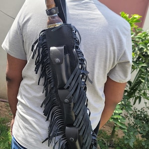 May include: A black leather sheath with a decorative wooden handle knife is carried over the shoulder. The sheath has a fringe design and two small pouches. The knife handle is brown with decorative metal accents.