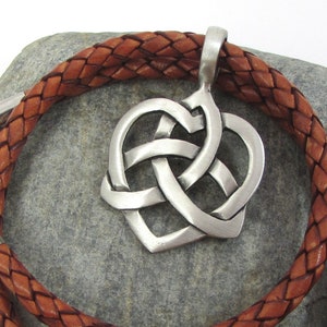 May include: A brown leather cord necklace with a silver Celtic knot heart pendant. The necklace is braided and has a lobster clasp closure.