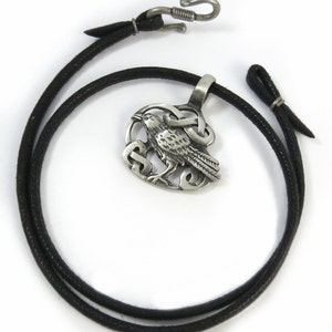 Pu&ograve; includere: Una collana d'argento con un ciondolo a nodo celtico e un design a corvo. La collana &egrave; su un cordoncino di cuoio nero.