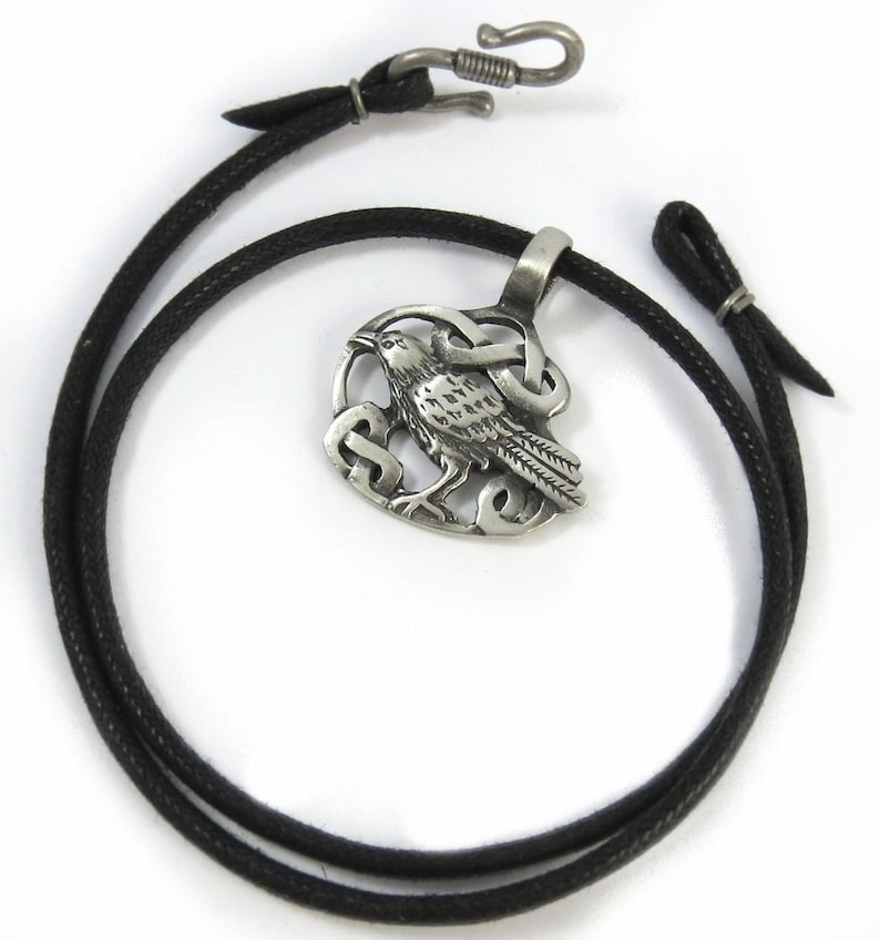 Pu&ograve; includere: Una collana d'argento con un ciondolo a nodo celtico e un design a corvo. La collana &egrave; su un cordoncino di cuoio nero.