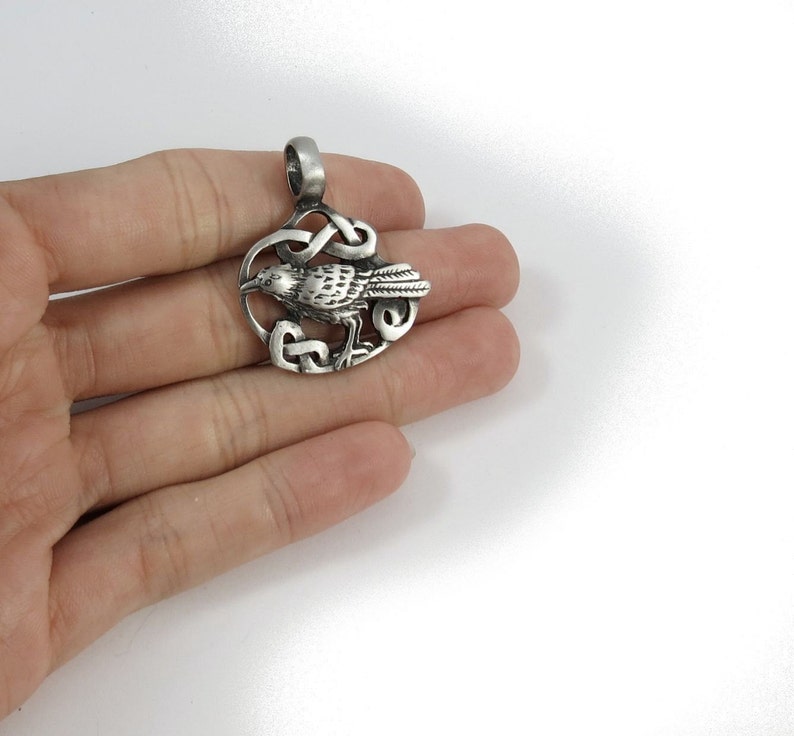 Pu&ograve; includere: Ciondolo in argento con un designo di corvo dettagliato all'interno di un nodo celtico. Il ciondolo &egrave; un simbolo celtico tradizionale di saggezza e conoscenza.