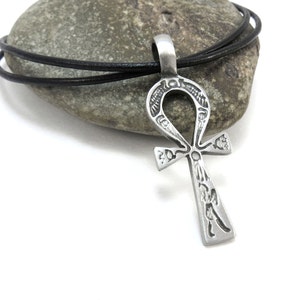 May include: A silver Ankh pendant with intricate details, hanging on a black leather cord. The pendant is a symbol of eternal life in ancient Egyptian mythology.
