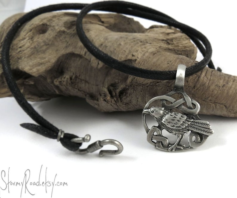 Pu&ograve; includere: Una collana con un ciondolo in argento che presenta un designo di corvo dettagliato con un nodo celtico. La collana &egrave; su un cordoncino nero con una chiusura a gancio in argento.