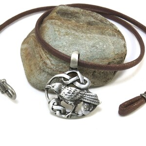 Pu&ograve; includere: Una collana con un ciondolo in argento con un designo a nodo celtico e un corvo. La collana &egrave; su un cordoncino in pelle marrone.