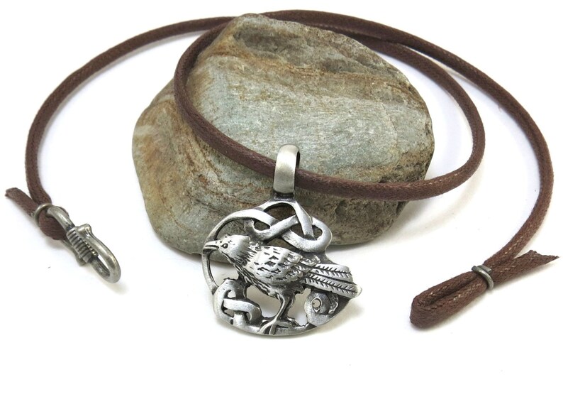 Pu&ograve; includere: Una collana con un ciondolo in argento con un designo a nodo celtico e un corvo. La collana &egrave; su un cordoncino in pelle marrone.