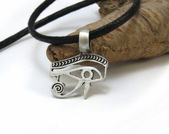 May include: Silver pendant necklace with an eye of Horus design. The pendant is on a black cord.