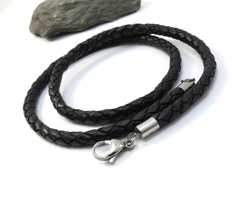 May include: Black leather cord necklace with a silver clasp. The cord is braided and has a smooth texture.