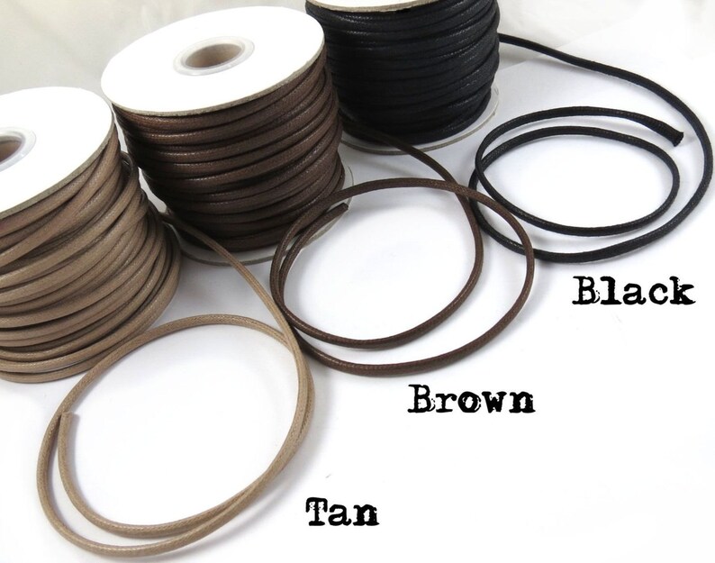 May include: Three spools of leather cord in tan, brown, and black. The cords are wound around white spools. The cords are shown in a circle around the spools.