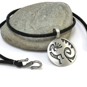 Könnte beinhalten: Eine silberne Halskette mit einem schwarzen Band. Der Anhänger ist rund und zeigt ein stilisiertes indianisches Design.