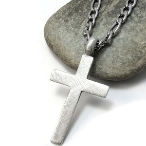 May include: A silver chain necklace with a brushed silver cross pendant.