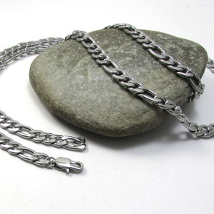 May include: Two silver curb chain necklaces with a box clasp closure. The chains are laying on a gray rock.