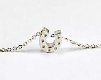 Puede incluir: Un collar de cadena de plata con un pequeño colgante de herradura texturizado.