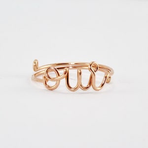 May include: A rose gold wire ring with the word "oui" spelled out in cursive.