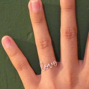 K&ouml;nnte beinhalten: Ein silberner Ring mit dem Wort "love" in Kursivschrift.