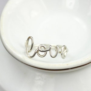 K&ouml;nnte beinhalten: Ein silberner Ring mit dem Wort "LOVE" in kursiv.