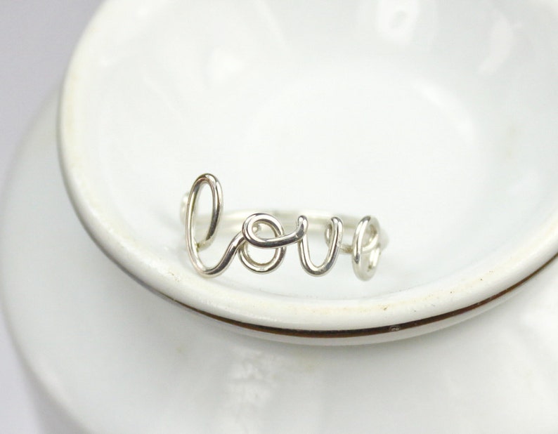 K&ouml;nnte beinhalten: Ein silberner Ring mit dem Wort "LOVE" in kursiv.