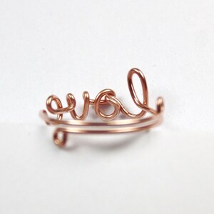 Puede incluir: Un anillo de alambre de color oro rosa con la palabra "love" escrita en cursiva.